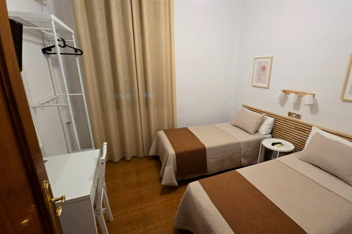 A hotel room with two beds, a small round table, a wardrobe, and a window with curtains.