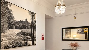 A lobby with two armchairs, a small table, a cabinet, a chandelier, and a large framed picture on the wall. - Hostal Prada (Madrid)