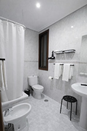 Un baño moderno con inodoro, bidé, lavamanos y un taburete pequeño.