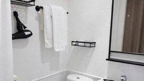 A small, modern bathroom with a toilet, sink, and mirror. There is a towel rack above the toilet and a trash can next to the sink. - Hostal Prada (Madrid)