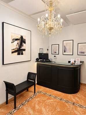Un espace d’accueil avec un bureau noir, un banc, un lustre et des œuvres d’art encadrées accrochées aux murs.