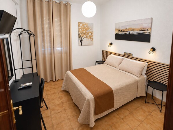 Une chambre d’hôtel avec un lit, un bureau équipé d’un ordinateur, une chaise, une lampe, un tableau accroché au mur et une fenêtre avec des rideaux.