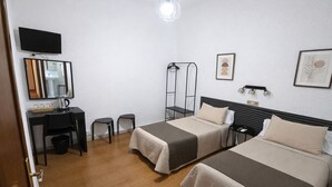 A hotel room with two beds, a desk with a chair, a TV, and a mirror. - Hostal Prada (Madrid)