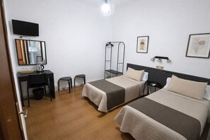 Una habitación de hotel con dos camas, un escritorio con silla, televisión y espejo.