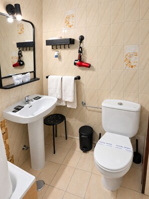 Une salle de bain avec un lavabo blanc, un miroir, des toilettes et une poubelle noire.