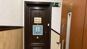 Entrada de un hotel con una puerta de madera oscura, un letrero que dice 'Hostal Prada' y una señal de 'No Entrar' encima.