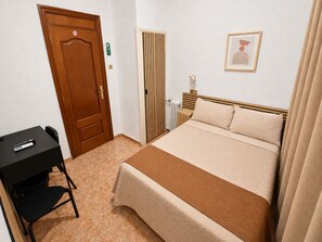 Une chambre d’hôtel avec un lit, un bureau et une chaise, un radiateur et un tableau encadré au mur.