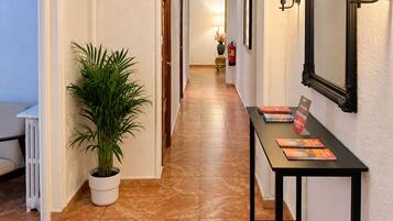 Pasillo de hotel con una planta en maceta, una mesa con folletos y un espejo con apliques de pared.
