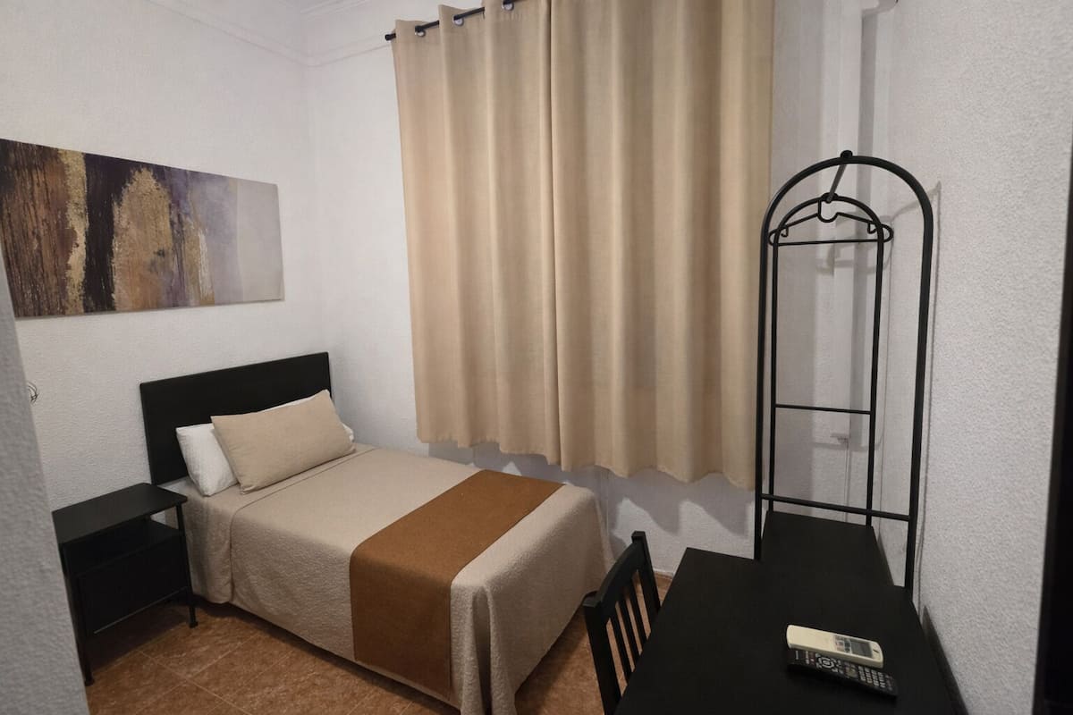 A bedroom with a bed, a nightstand, a table with a remote control, and a hanging chair.