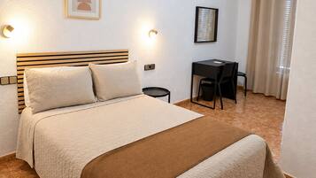 Una habitación de hotel con una cama, lámparas de noche, un escritorio y una silla.