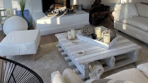 Un salon moderne avec une cheminée, des canapés blancs, une table basse avec des bougies et une lampe rouge.