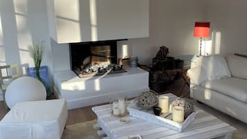 A modern living room with a fireplace, white sofas, a coffee table with candles, and a red lamp.