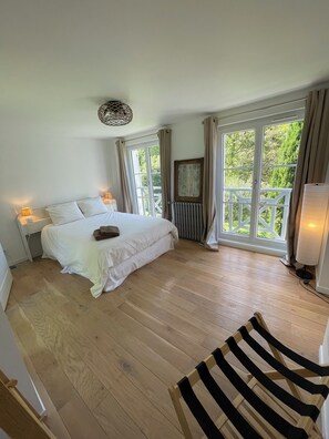 Ein Schlafzimmer mit Bett, Nachttischlampen, Heizkörper und großen Fenstern mit Vorhängen.