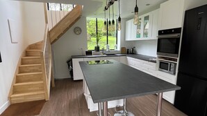 Une cuisine moderne dotée d’un îlot central, d’appareils électroménagers en acier inoxydable et d’un escalier en bois.
