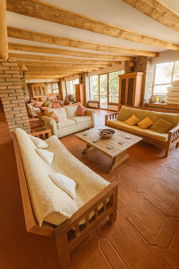 Un amplio salón con muebles de madera, chimenea de piedra y grandes ventanales que ofrecen vistas al exterior.