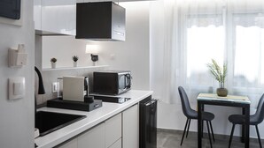 A modern kitchen with white cabinets, a microwave, and a dining area with a table and chairs. - Athens Praxitelous Vibes (Athina)
