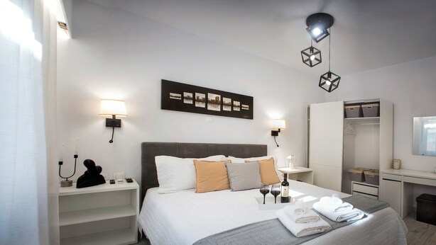 A neatly arranged hotel room with a large bed, bedside tables, a wardrobe, and a desk with a mirror. - Athens Praxitelous Vibes (Athina)