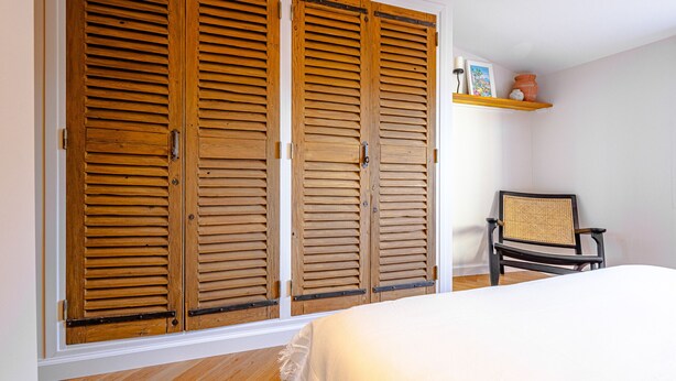 Un dormitorio con cama, puertas correderas de madera, una silla y una estantería con objetos decorativos.