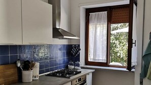 Una cucina compatta con mobili bianchi, un fornello a gas, un forno e una finestra con vista sul verde.