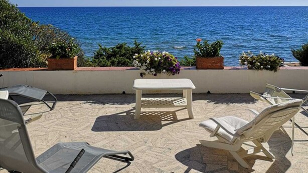 Una terrazza con vista sul mare, con due poltrone, un tavolino e piante in vaso.
