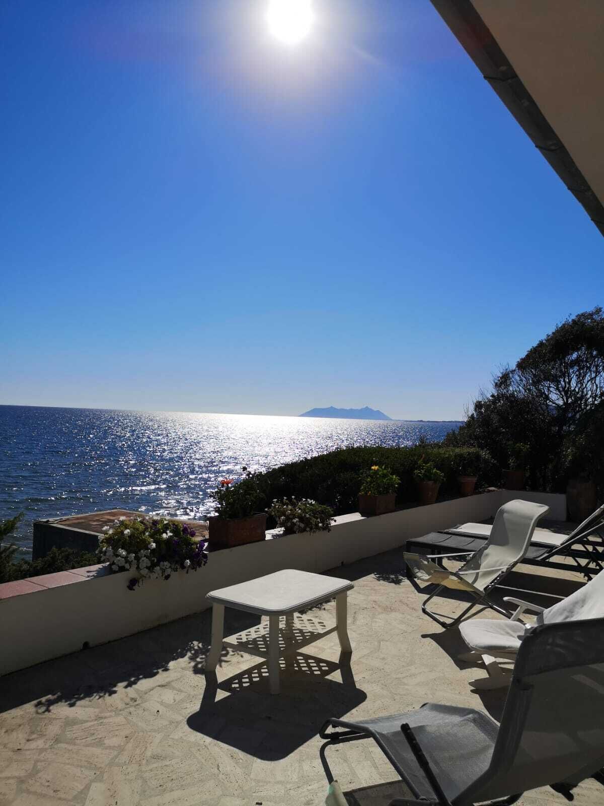 Una terraza con vista al mar, una mesa y dos sillones de descanso.