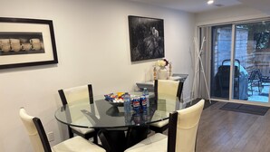 Zona pranzo moderna con tavolo in vetro circondato da sedie, un quadro appeso al muro e vista sull'esterno.