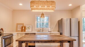 A kitchen with a wooden table, stainless steel appliances, a large window, and a woven pendant light. - Walk to Main St & Swamp Rabbit Trail (Travelers Rest)