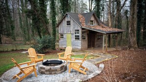 A rustic cabin with a fire pit and Adirondack chairs in a wooded area. - Walk to Main St & Swamp Rabbit Trail (Travelers Rest)