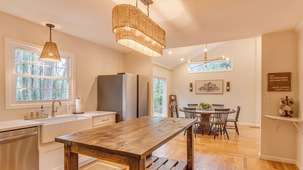A modern kitchen with a wooden table, stainless steel appliances, and a hanging light fixture. - Walk to Main St & Swamp Rabbit Trail (Travelers Rest)