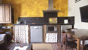 Une cuisine compacte équipée d’un lave-vaisselle, d’un four à micro-ondes et d’un grille-pain. On y trouve une table à manger avec des chaises, ainsi qu’un téléviseur fixé au mur.