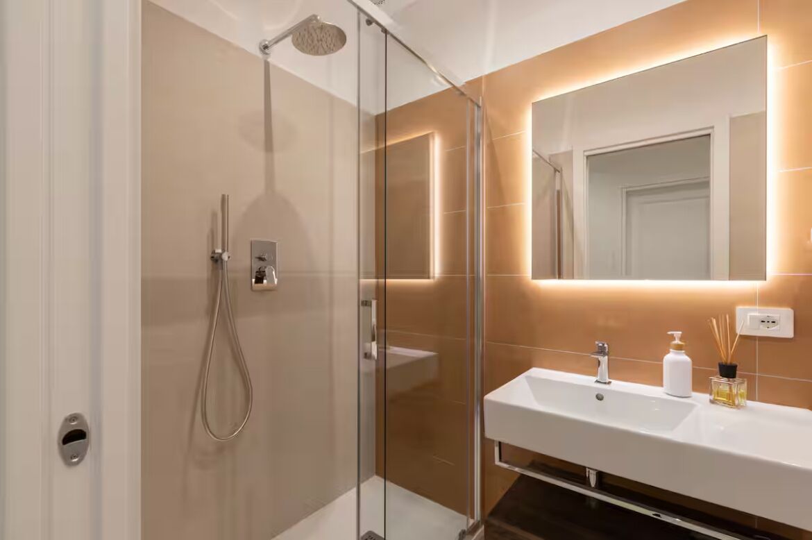 Une salle de bain moderne dotée d’une douche à parois de verre, d’un lavabo blanc et d’un miroir avec éclairage intégré.