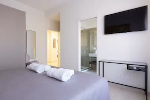 A modern hotel room with a bed, a TV mounted on the wall, and a desk with a mirror.