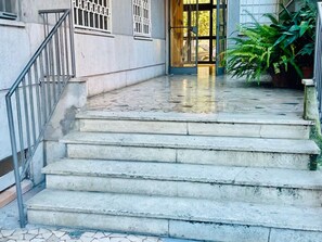 A set of concrete steps leading to a building entrance with a metal railing on the left.