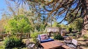 Un espace extérieur aménagé avec un banc en pierre, une table en bois et deux chaises pliantes.
