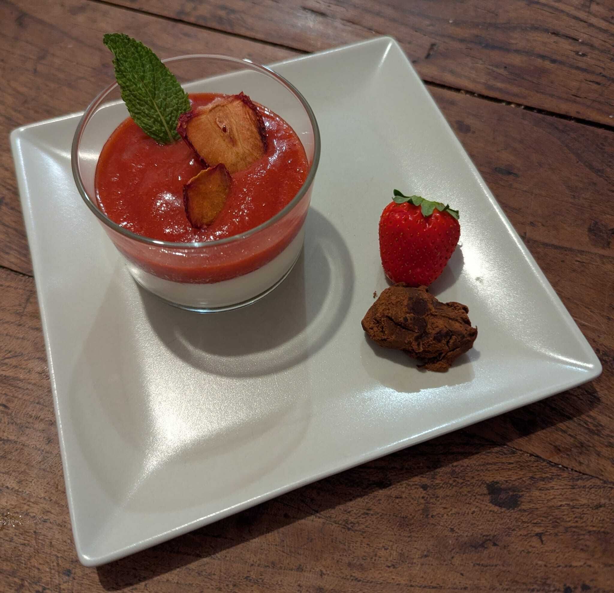 Un dessert con guarnizione di fragola e menta su un piatto bianco.