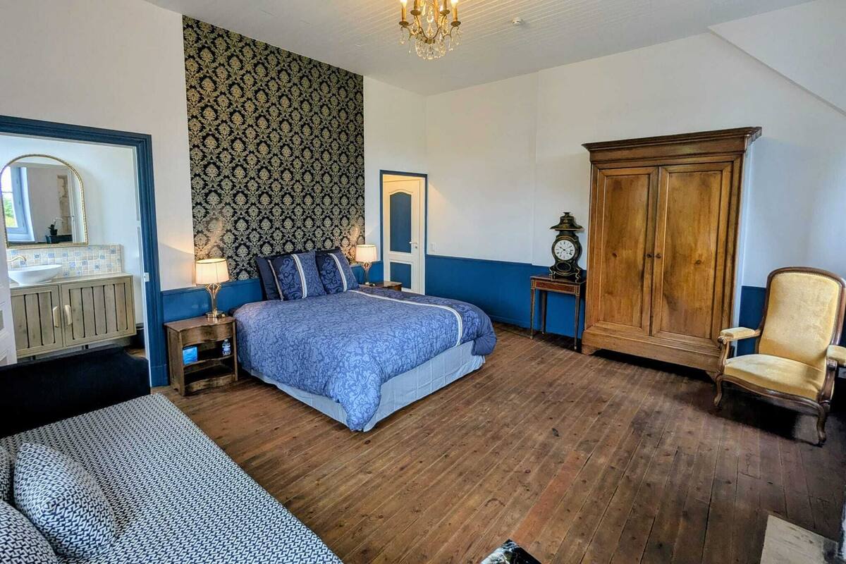 Een slaapkamer met een bed, een houten garderobe, stoel, nachtkastje en een spiegel.