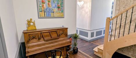 A piano, a chair, a potted plant, and a staircase in a room with wooden floors and a painting on the wall.