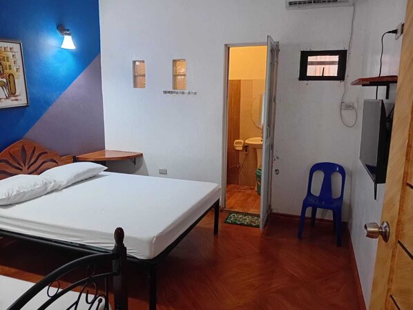 A bedroom with a bed, a wooden headboard, a nightstand, a blue chair, and a bathroom visible through an open door. - oyo187 Rose Ros Place Budget HotelResort (Santo Tomas)