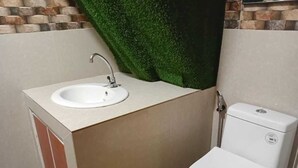 Ein kleines Badezimmer mit einem weißen Waschbecken und einer Toilette, beige Wänden und einer Wand mit Kunstgrase in Grün.