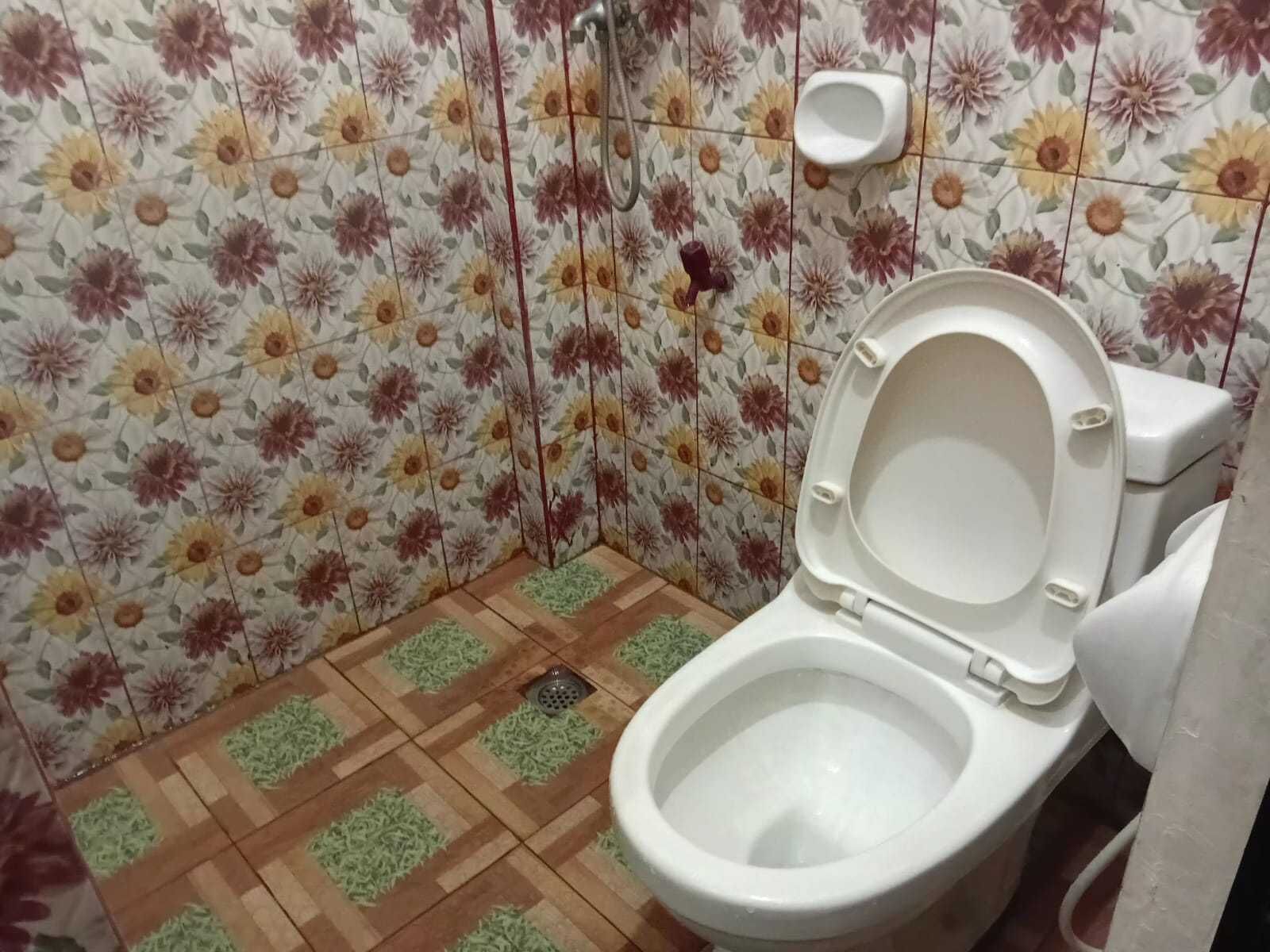 A bathroom with a toilet, a shower, and a urinal. The walls are tiled with a floral pattern.