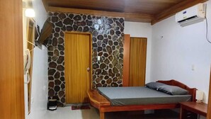 Ein Schlafzimmer mit Steinwand, Holztür und einem Bett mit grauem Matratze.