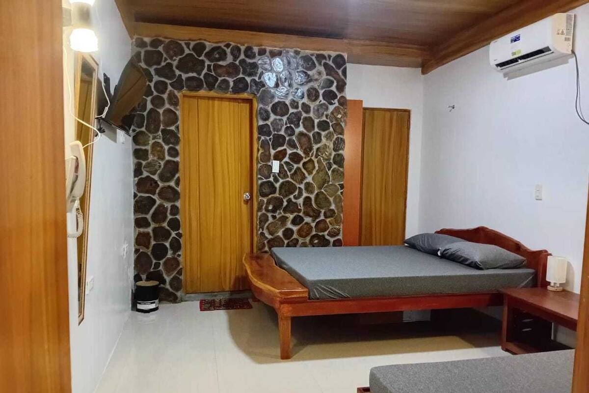 Une chambre avec un mur en pierre, une porte en bois et un lit doté d’un matelas gris.