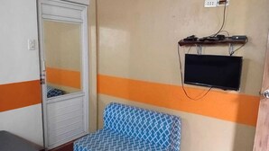 Ein Zimmer mit geschlossener Tür, einem gemusterten blauen Sessel, einem an der Wand befestigten Fernseher und einer Steckdose.