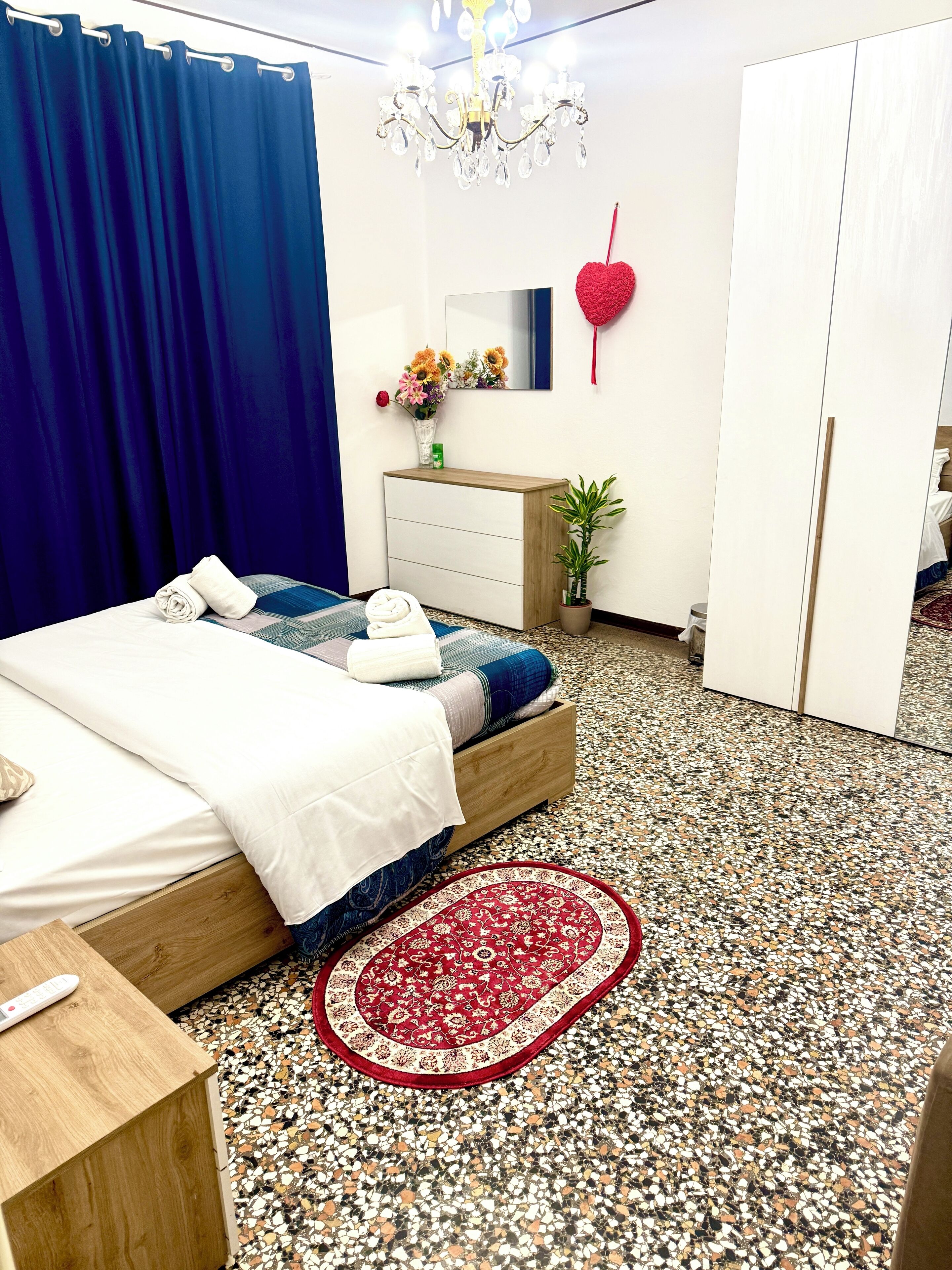 Une chambre à coucher avec un lit, une commode en bois, un tapis rouge, une plante en pot et un miroir au mur.