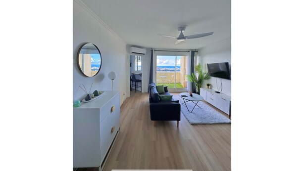A modern living room with a sofa, a TV, and a ceiling fan. There is a large window with a view of the outdoors. - La Verrière with its panoramic view! (Saint-Denis)