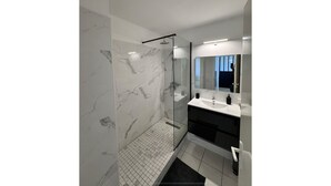 A modern bathroom with a glass-enclosed shower, white marble walls, a black sink, and a large mirror. - La Verrière with its panoramic view! (Saint-Denis)