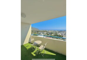 Ein Balkon mit Meer- und Stadtblick, ein kleiner Tisch und zwei Stühle.
