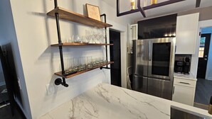 A kitchen with a stainless steel refrigerator, marble countertop, and wooden shelves holding glasses. - Fabulous 3-bedrm In town/Masters 1 mle Bungalow new VRBO & SUPERhost on Air BB (Augusta)
