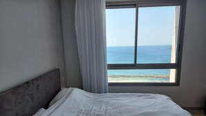 A bedroom with a bed, a window with a view of the sea, and a curtain.
