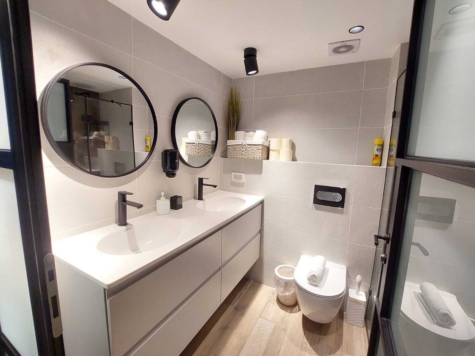 A modern bathroom with two sinks, a toilet, and a shower area.